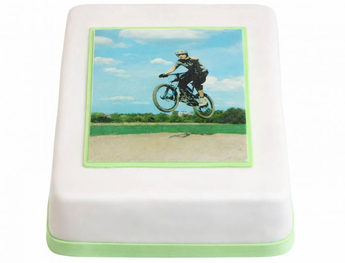 Weiße rechteckige Fototorte mit essbarem Foto eines Jungen auf dem Fahrrad und grünem Rand für Geburtstag oder Konfirmation